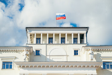 Naklejka premium classical building with a prominent Russian flag flying from the roof. The setting features a blue sky scattered with clouds, highlighting the architectural details