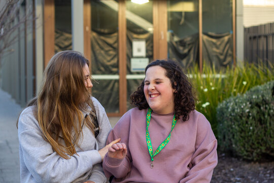 Two young women walking on an urban street sharing a warm, friendly moment