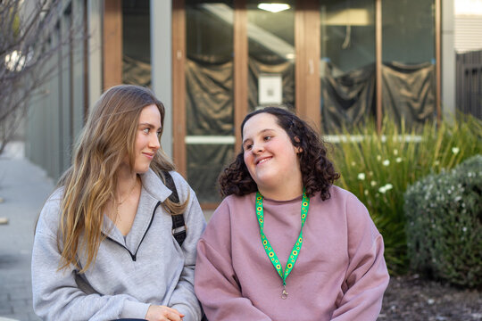 Two young women walking on an urban street sharing a warm, friendly moment