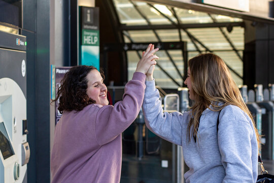 Two women standing beside a public transport card top-up machine doing high-five