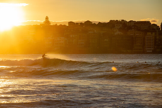 Surfer riding a breaking ocean wave at golden sunset with seaside town in background