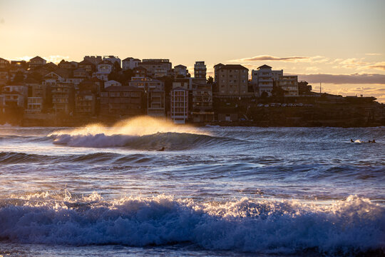 Surfers waiting beyond the breaking waves, while the densely developed headland rises prominently