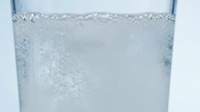 Effervescent tablet dissolving in a clear glass of water, releasing bubbles, fizzing chemical reaction, healthcare and medicine