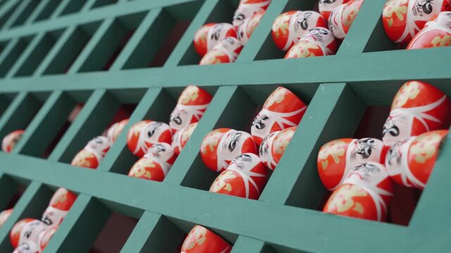 Rows of hundreds traditional Daruma dolls are arranged on green wooden shelves at Katsuoji Temple in Osaka, Japan, representing Japanese traditions of good fortune, perseverance, wishes, and success.