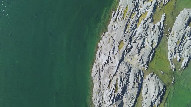 Top down aerial drone shot capturing boundary where smooth white granite bedrock meets clear green waters of Sylvia Grinnell estuary