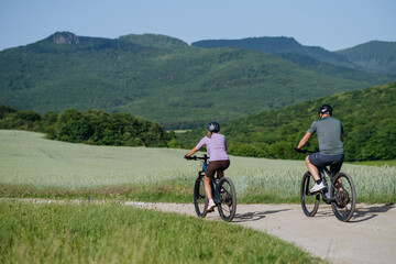 Fototapeta premium Happy mature couple riding e-bikes through scenic countryside.
