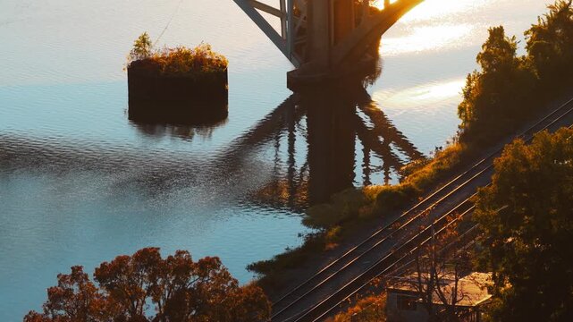 Concrete bridge arch glows in low sunlight above reflective water in Ozark, Arkansas along the river with perfect symmetrical reflection of support beams, tilt upward