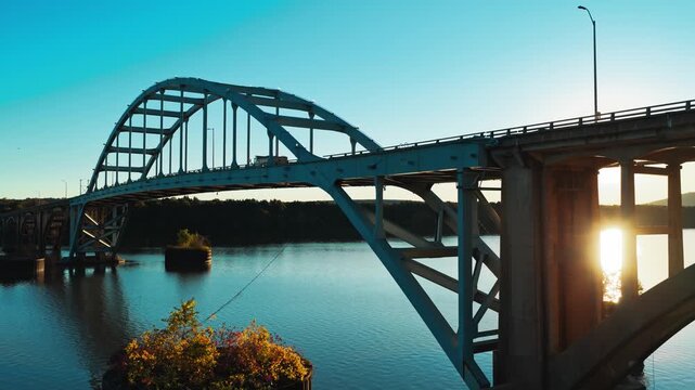 White and concrete bridge arches span calm river in golden light at Ozark, Arkansas, low aerial tracking left as sunset glistens between beams