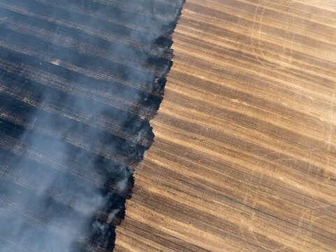 Field fire from above, smoke rising, soil textures contrasting