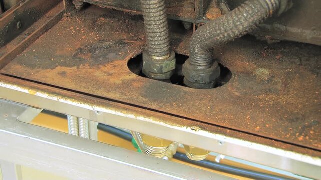 Close view of a deeply corroded metal surface revealing intricate electrical conduits and robust nuts in an abandoned industrial setting.