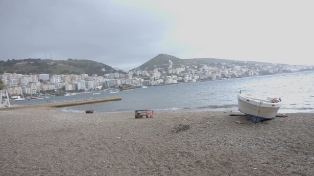 Panning Shot of a Fishing Boat on a Sandy Beach Facing Saranda Cityscape and Bay, Albania