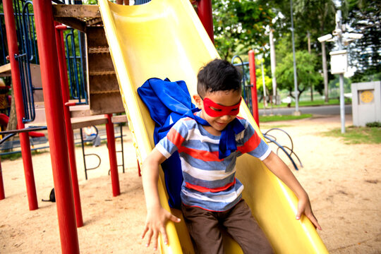 Child in superhero costume sliding down a playground slide.