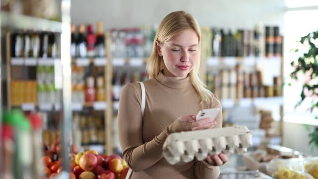 Before buying, girl scans barcode QR code on eggs label package, follows link and studies information for consumer in supermarket application 