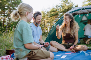 Naklejka premium Happy family playing cards during summer camping trip.