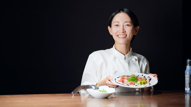 料理を持つ女性シェフ。調理師、レストラン、飲食店、料理、フレンチ、イタリアン、ディナー、完成、提供