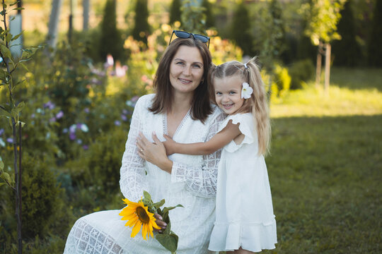 a cute five-year-old girl with mother in a white dress are playing in a green summer garden. happy childhood