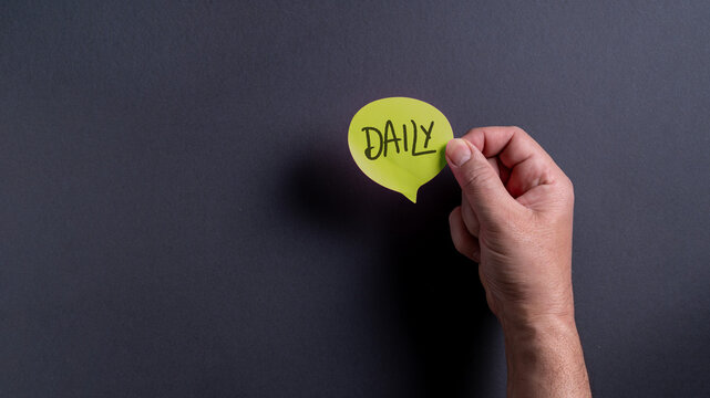 Male hand holding yellow speech bubble with daily text on dark background