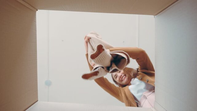 Low angle view of surprised young asian woman unpacking. Opening carton box and looking inside. Packaging box, delivery service. Human emotions and facial expression