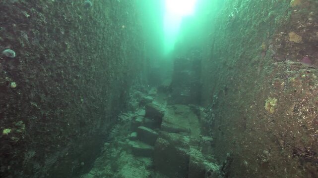Journey descends into the Barents Sea's profound rock formations. Glimmering sunlight penetrates the depths, illuminating an underwater cave habitat.