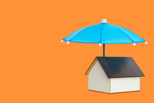Insurance. House model sits under colorful umbrella, symbolizing protection