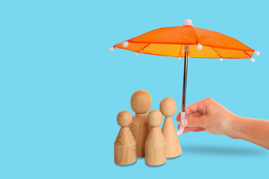 Insurance. Hand holds orange umbrella above wooden figures representing security and safety