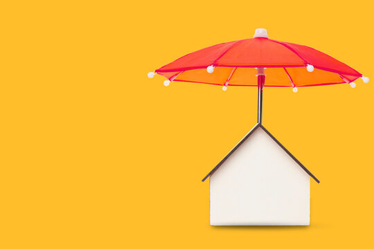 Insurance. Model house sits under a red umbrella on bright background. Insurance protection concept