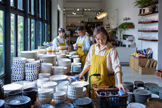 Asian employee is examine her new ceramics shelf of bowl, plate, cutlery and utensil in local artisan handmade store for handcraft and products for part time job concept