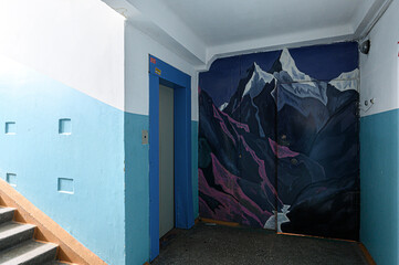 Stairwell with dramatic mountain mural on wall. pale blue and white walls, blue door frame, concrete steps, and utilitarian urban aesthetic © evgeniykleymenov