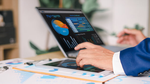 Analyzing digital dashboards on a tablet and laptop, using charts, statistics, and performance data for financial planning, market research.