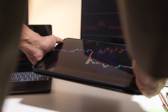 Professional financial analyst reviewing stock market charts across multiple screens using a tablet, laptop and calculator to evaluate price movements, technical indicators, and investment strategies.