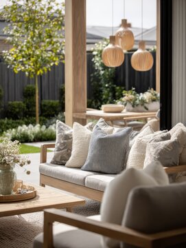Open living area with neutral sofa, layered cushions, natural wood furniture and pendant lighting beside a sunny garden, designed for contemporary home inspiration and relaxed indoor outdoor living.