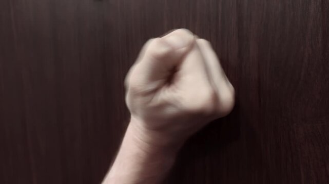 Fist knocks on front door. Close up shot man fist knocking on front wooden door entrance. Person wants to gain access home or office building. Urgent request entry.