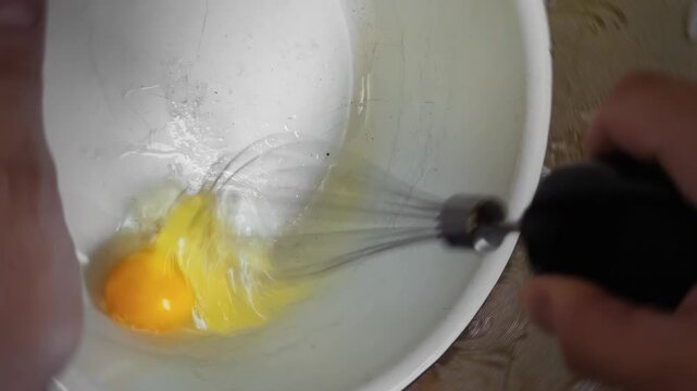Man uses whisk to beat raw egg in soviet large metal bowl to make omelet. Preparing ingredient for omelette, breakfast meal preparation, culinary process, making food