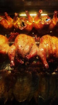 Vertical 4K slow motion footage of multiple chickens rotating in a hot rotisserie oven, showing perfectly cooked meat with oil slowly dripping.
