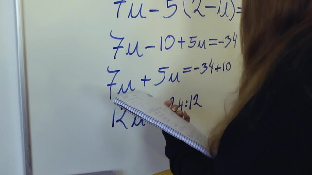 Female high school student with a notebook solving a complicated algebraic equation on a whiteboard with a blue marker during a mathematics class, demonstrating her problem solving skills