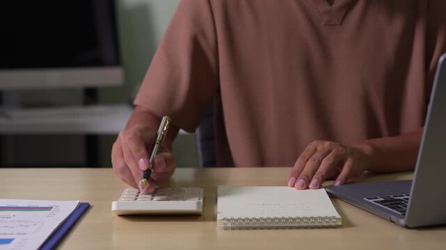 Male use a laptop computer and take notes in the notebook at the office desk.