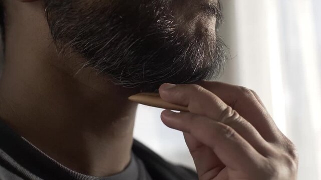 Man grooming beard and mustache with wooden comb, close up shot.