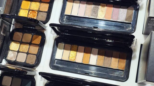 Multiple open eyeshadow palettes display various shades warm earth tones cool grays shimmers professional cosmetic product makeup collection beauty retail store presentation