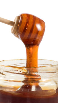 Honey dripping from a wooden dipper into a glass jar filled with honey