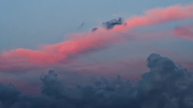 Pink light on elongated cloud formation across sky with dark cumuliform clouds below, twilight atmosphere, tranquil natural environment, sky landscape, weather patterns. Sunset sundown dusk