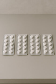 White round tablets in four blister packs arranged on smooth beige surface, representing healthcare, medicine, and pharmaceutical concepts with clean and minimalistic background