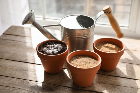 A watering can beside three pots where only one has damp soil