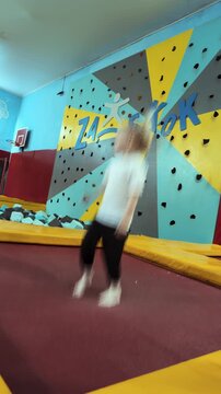 Little Caucasian girl with pigtails jumps high with energy on trampoline platform. Child experiences joy and active play at indoor trampoline park. Happy childhood. Four-year-old kid. Vertical shot