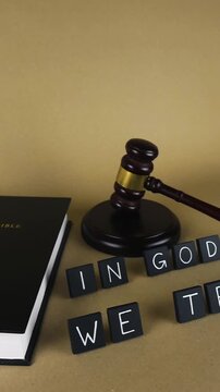 Holy Bible lying next to a judge's gavel and the official motto of the United States, In God We Trust, spelled out in letter tiles, representing the intersection of law, justice, and faith