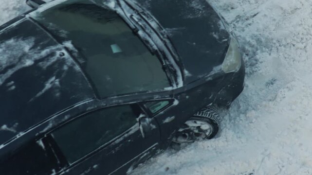 Dark color car stuck in deep winter snow on roadside after heavy snowfall during cold weather day with tire marks visible