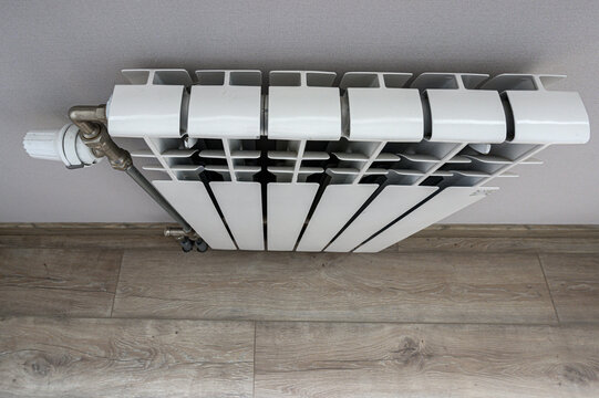 white bimetallic radiator features vertical panels, top convection fins, side-mounted thermostatic valve. set against neutral wall with light-wood flooring