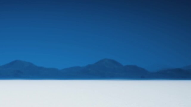 Mountains are seen in the distance under a clear blue sky. The ground is white, creating a stark contrast with the blue and the mountains. The scene appears bright and open.