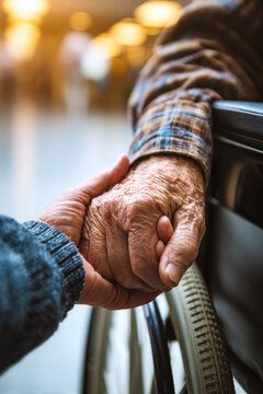 Elderly man in wheelchair holds the hand of a young man in a hospital. The scene captures a moment of support and connection between them