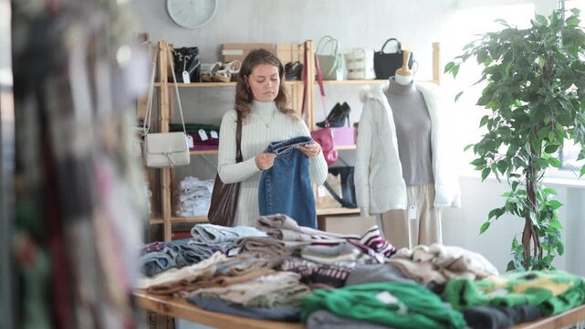 Happy young girl choosing jeans trousers in clothing shop with new winter collection 