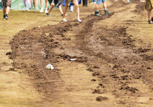 People walk along muddy, uneven ground at outdoor event